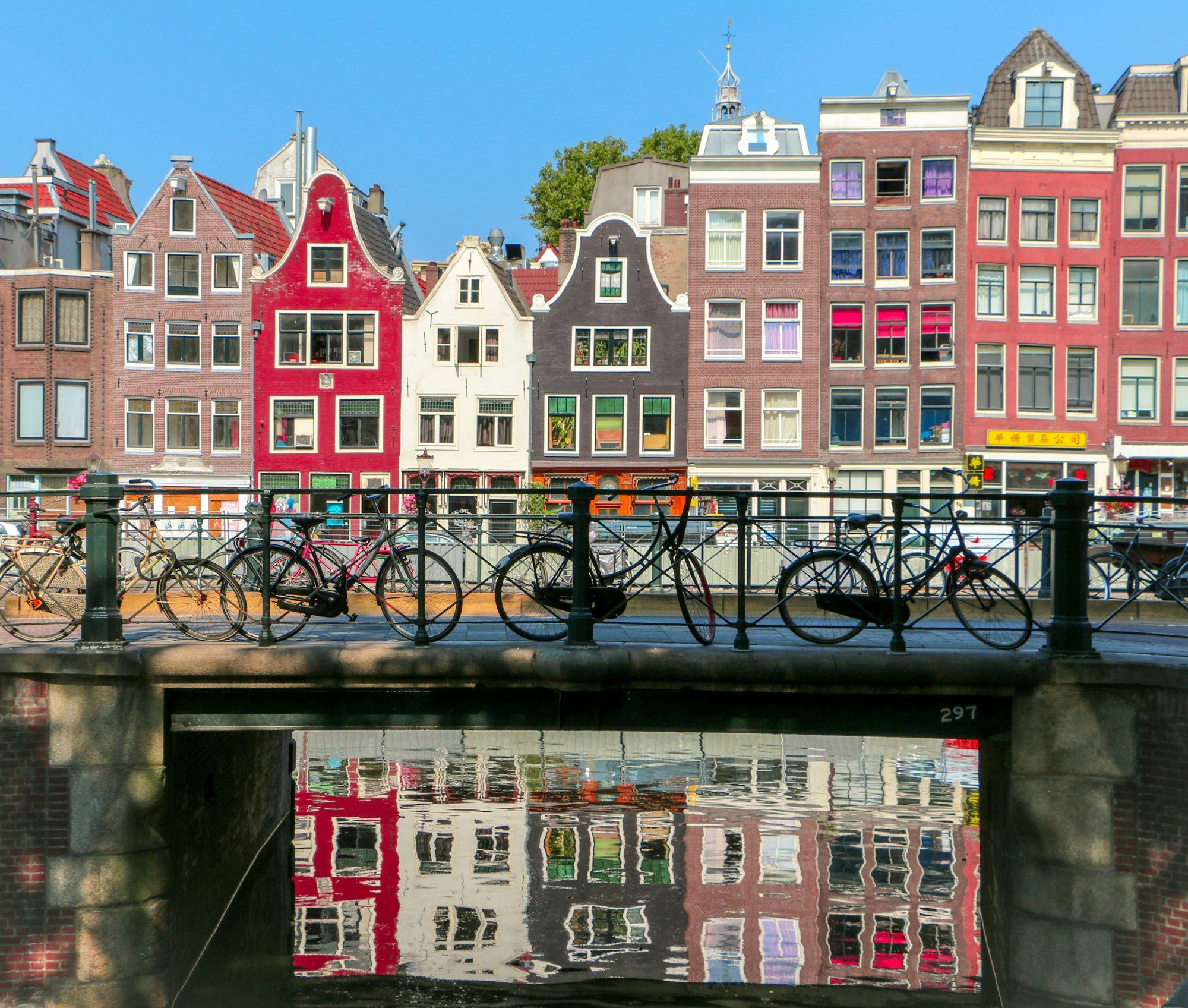 Bicycles parked on a canal bridge in front of tall Amsterdam houses