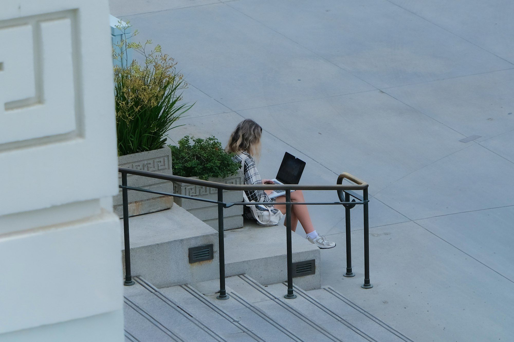 A woman working on a laptop, sitting on sunny steps outdoors